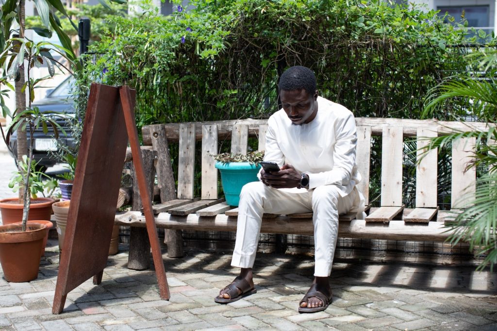 Photo of an African man sitting on a bench using a mobile phone. 
