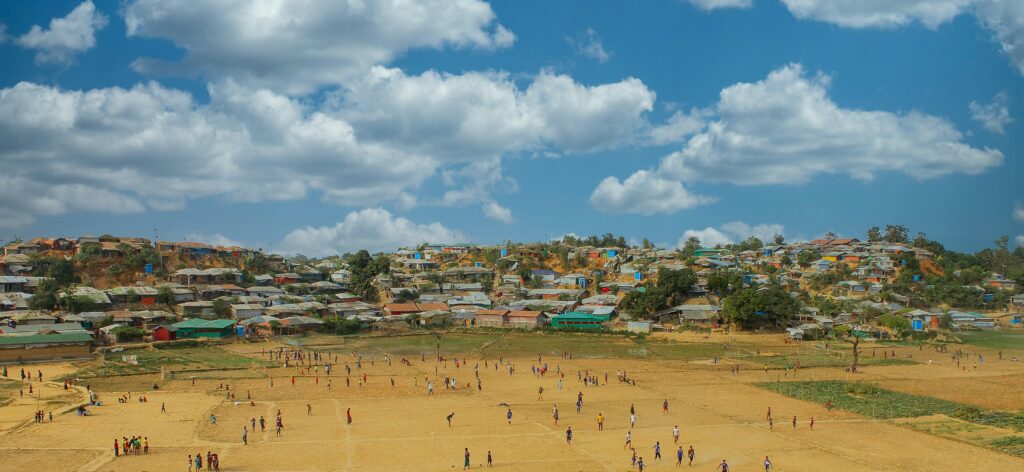 Image shows individuals in a field in front of Balukhali camp, Ukhiya, Cox's Bazar.